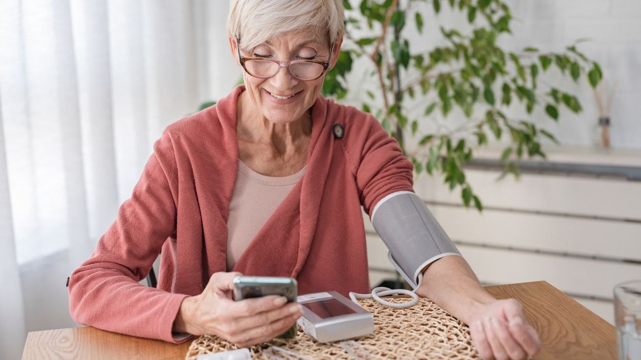Older woman Measuring her blood pressure in the comfort of her own home while still receiving care from a qualified care team via her phone
